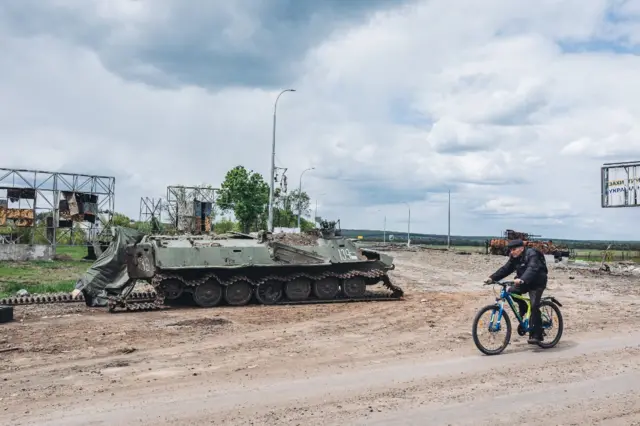 A man cycles past a damaged Russian tank