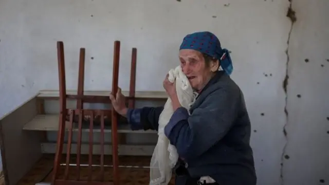 Woman stands in her damaged house in Komyshuvakha