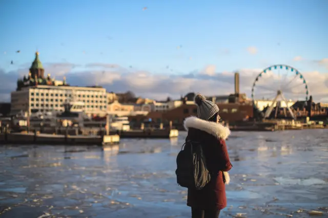 Young woman standing in front of frozen ice with South Harbour urban skyline, Helsinki, Finland