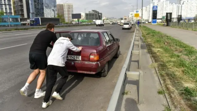 Motorists push their vehicle in a queue at a petrol station in Kyiv Ukraine