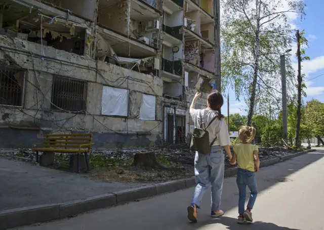 A local woman and a girl walk past a residential building damaged during shelling in Kharkiv,