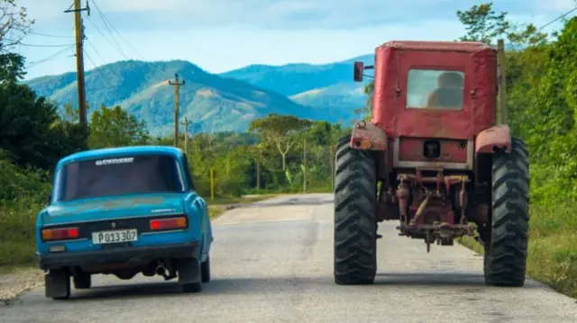 A Moskvich passes a tractor on a Cuban road