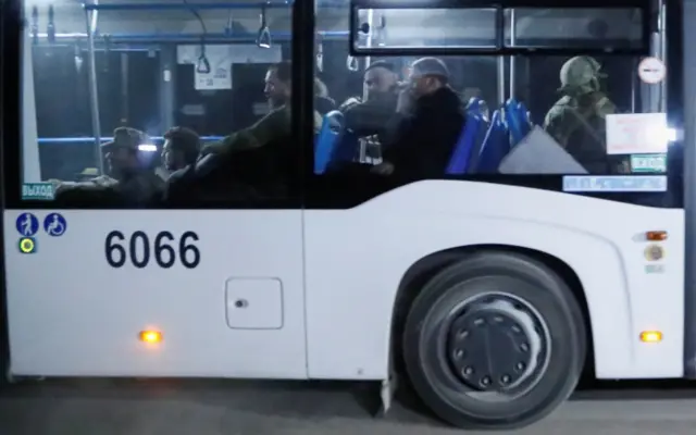 A bus carrying service members of Ukrainian forces from the besieged Azovstal steel works drives away under escort of the pro-Russian military