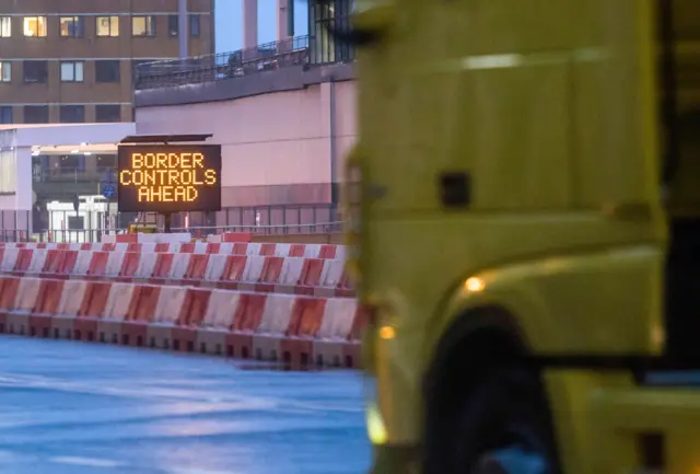 A lorry approaches a road sign that says 'Border checks ahead'