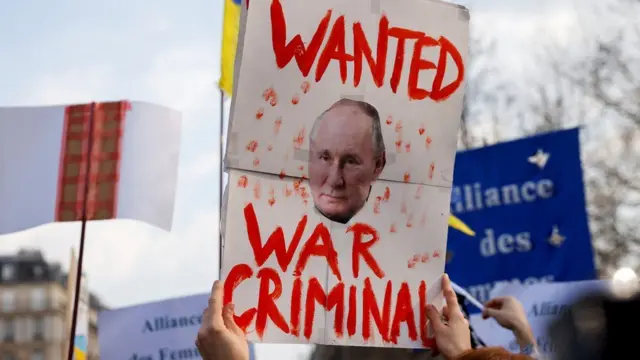 A protest sign showing Vladimir Putin's face alongside the message "Wanted War Criminal"