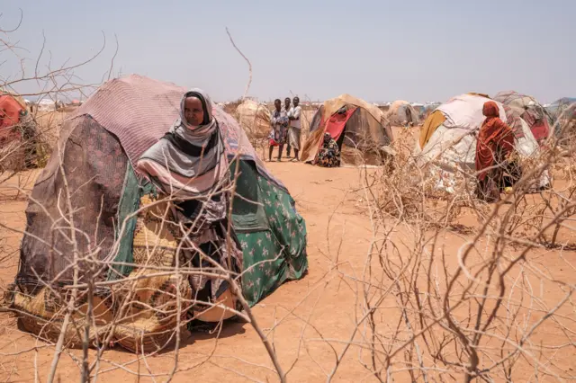 People stand next to tents in the camp for internally displaced people of Farburo 2 in the village of Adlale, near the city of Gode, Ethiopia, on April 6, 2022.