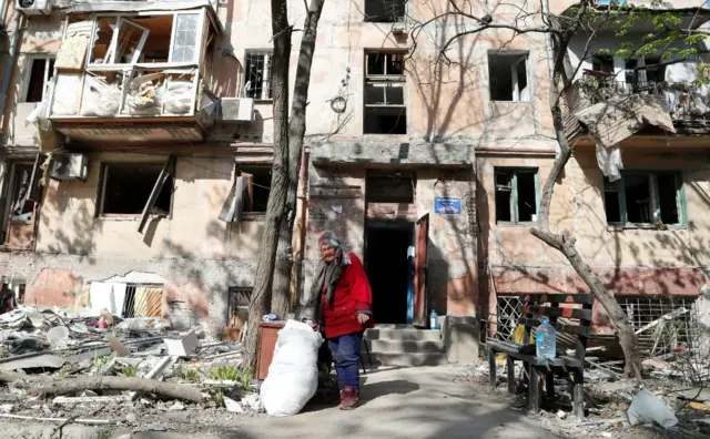 A woman stands near a heavily damaged building in Mariupol