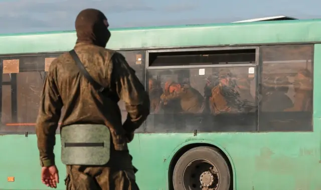 A service member of pro-Russian troops stands guard on a road near a bus carrying Ukrainian soldiers, who surrendered at the besieged Azovstal steelworks near Mariupol, Ukraine, on 20 May 2022