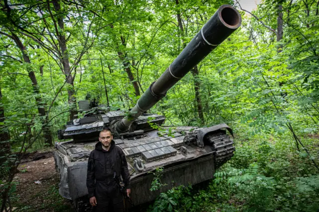 A Ukrainian soldier poses with his tank in woodland