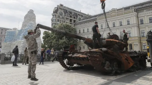 Workers remove debris from a destroyed Russian tank at the Mikhailovsaya Square in Kyiv, Ukraine