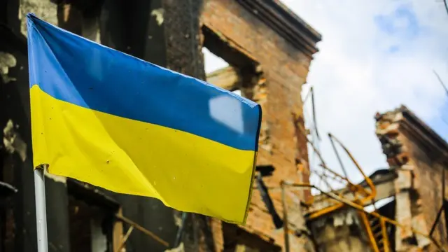 A Ukrainian flag flies in front of a damaged building