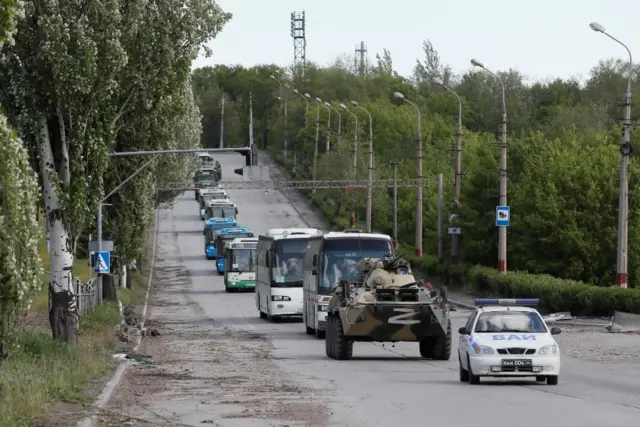 A Russian armoured vehicle drives in front of a convoy of coaches carrying Azovstal fighters