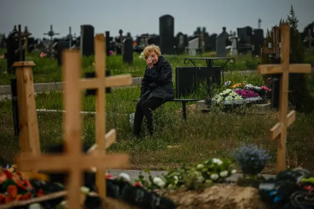 An elderly woman mourns while visiting the grave of a Ukrainian serviceman killed during the war