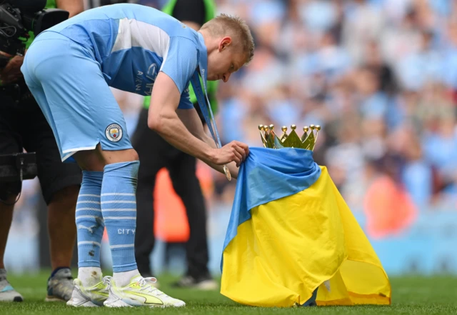 Oleksandr Zinchenko drapes the Ukrainian flag around the Premier League trophy