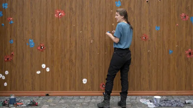 Artist paints flowers on bullet holes in a fence in Bucha