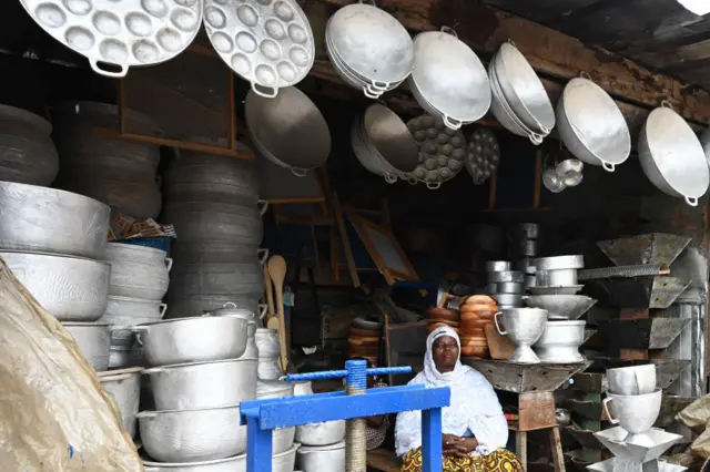 Woman sitting at market stall with pots and pans
