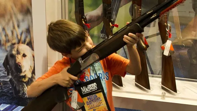 A child inspects a shotgun at the NRA's 2015 conference