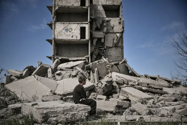 A young boy sits in front of a damaged building after a strike in Kramatorsk in the Donbas region