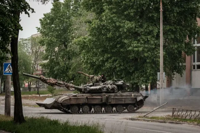 A Ukrainian main battle tank drives on a street during nearby mortar shelling in Severodonetsk