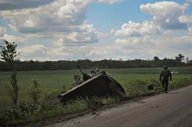 A Ukrainian serviceman walks next to a damaged armoured vehicle