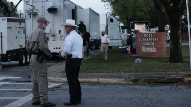 People and media trucks outside Robb Elementary School