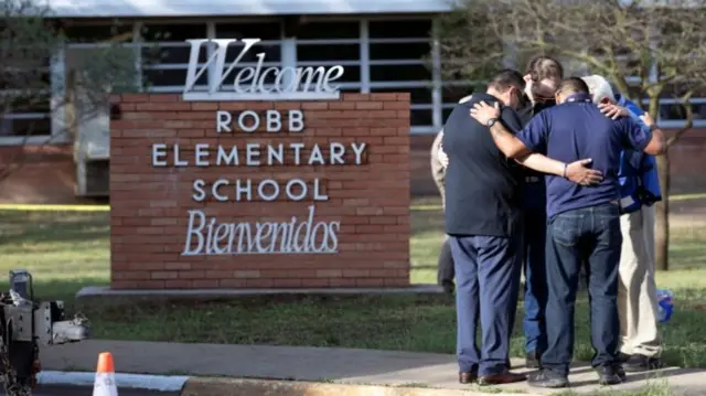 People with their arms around each other outside Robb Elementary School, Uvalde