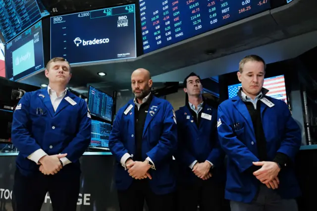 Traders on the floor of the New York Stock Exchange observe a moment of silence before the trading day begins