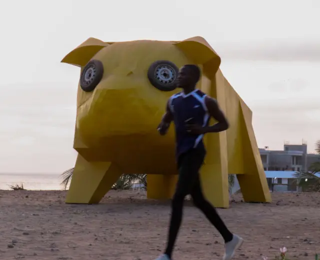 A man running past a contemporary yellow sculpture in Dakar, Senegal