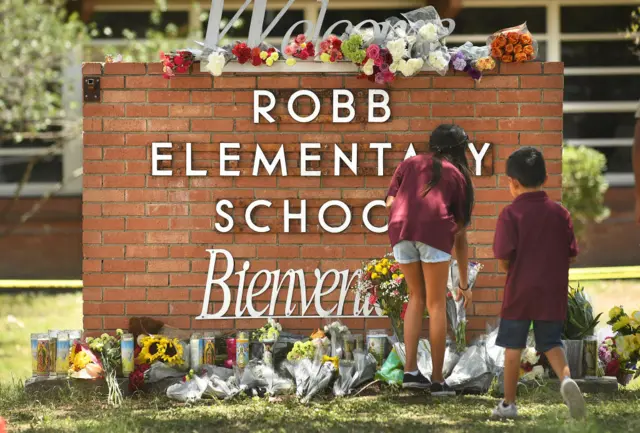 The siblings of a murdered child place flowers at a makeshift memorial outside the school