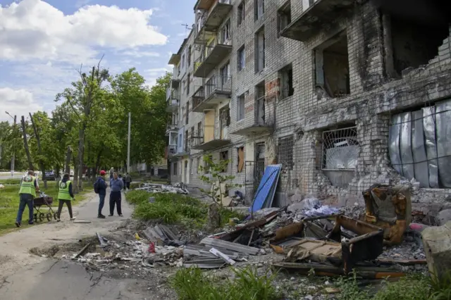Locals walk past a building that was damaged during shelling on the outskirts of Kharkiv, Ukraine, on 25 May 2022