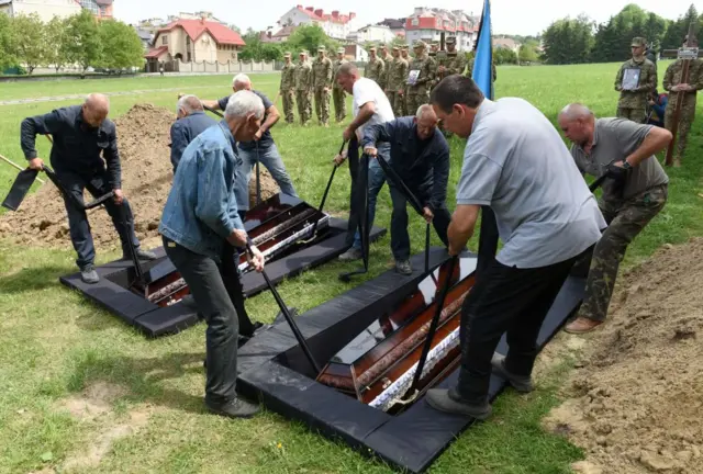Employees put down the coffins of Andriy Vertiev and Serhiy Evtushenko, Ukrainian servicemen, killed during the Russian invasion of Ukraine, during funeral at Lychakiv cemetery in the western Ukrainian city of Lviv, on May 25, 2022