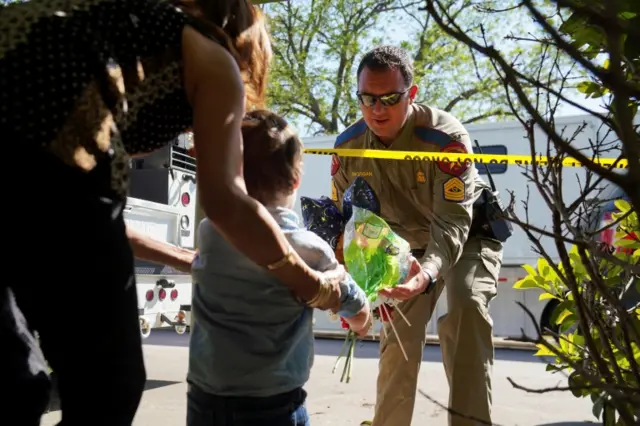 A local child hands flowers to an officer outside the school to add to the growing memorial site