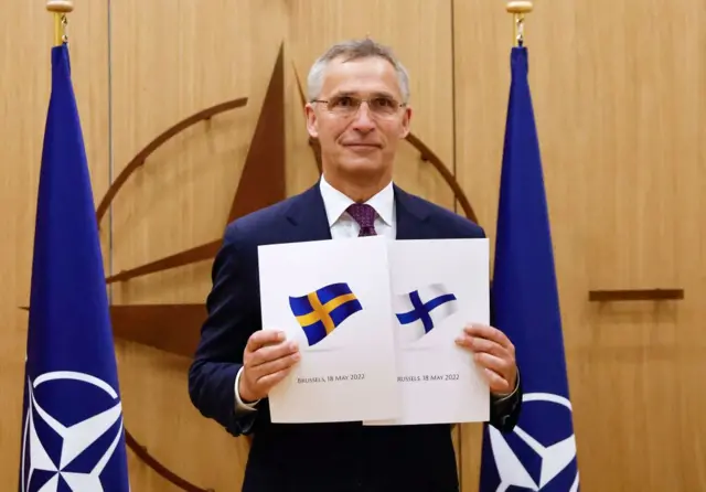 Image shows Jens Stoltenberg holding up two documents