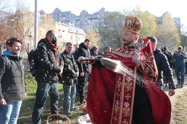 A priest blesses people and their baskets with holy water during the Orthodox Easter celebrations in the town of Bucha largely destroyed by Russian forces. Photo: 24 April 2022