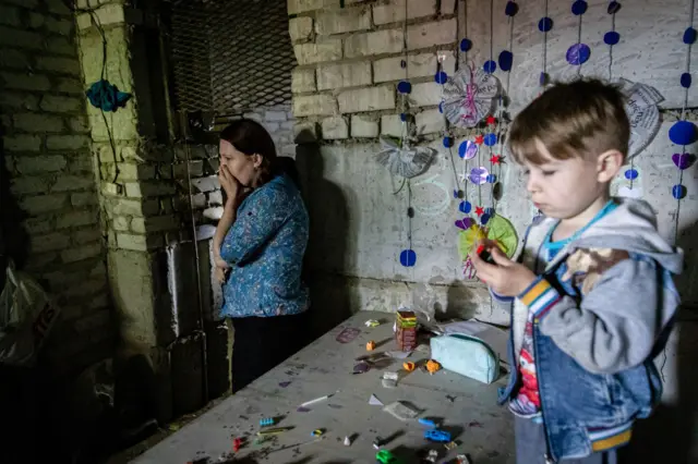 A mother is seen crying as her son plays with toys at an underground bomb shelter in Lysychansk in Luhansk