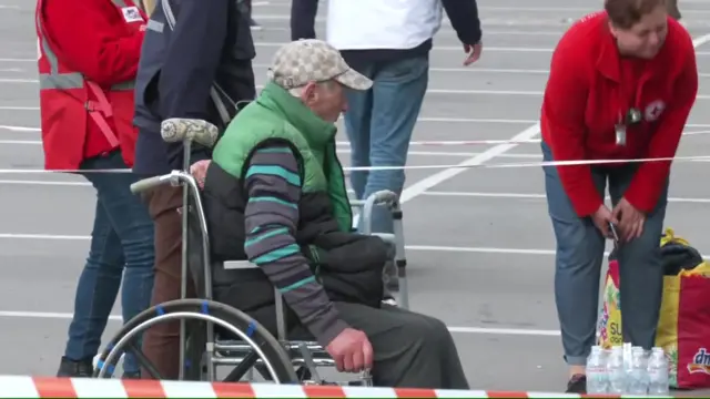 An elderly man is given assistance by Red Cross staff once off the bus