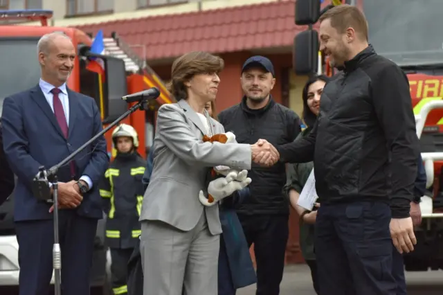 French Foreign Minister Catherine Colonna (C) is presented with a toy service dog by Denys Monastyrky (R), Ukrainian minister of interior ministry, during a showcase of ambulances and fire engines donated by France, in Kyiv, Ukraine, 30 May 2022