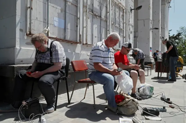 People charge their electronic devices in front of a theatre destroyed during Ukraine-Russia conflict in the port city of Mariupol