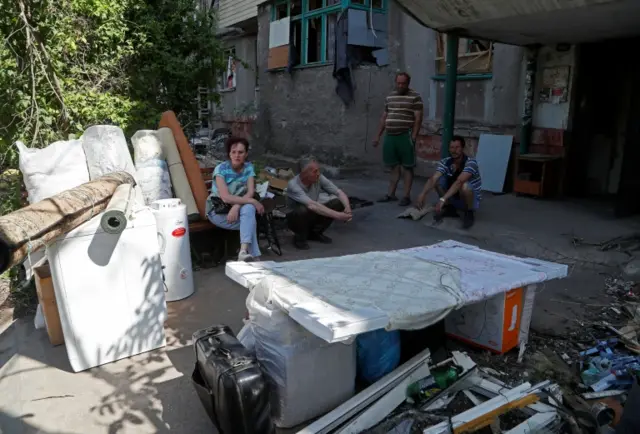 Mariupol residents sit next to their belongings stacked in front of an apartment building before their departure