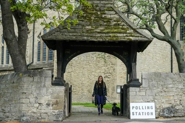 A woman walks near a polling station sign in a churchyard