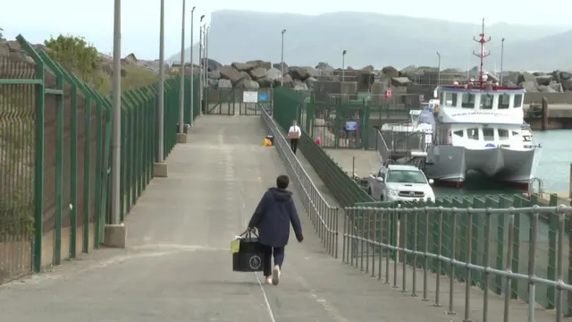 A person walks with a ballot box in hand towards the jetty in Ballycastle