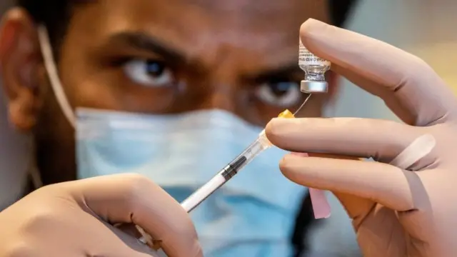 A medic extract a Covid vaccine dose from a vial.