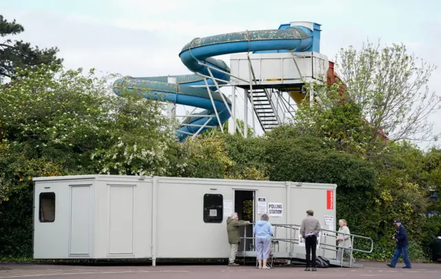 People queue outside a mobile polling station in front of a blue water slide