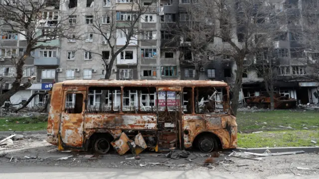 A burnt out bus in front of a residential building damaged in Mariupol