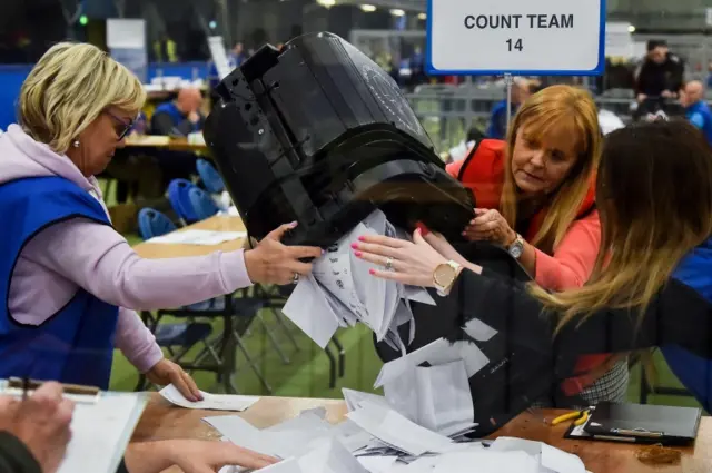 Electoral officers empty a ballot box onto a table