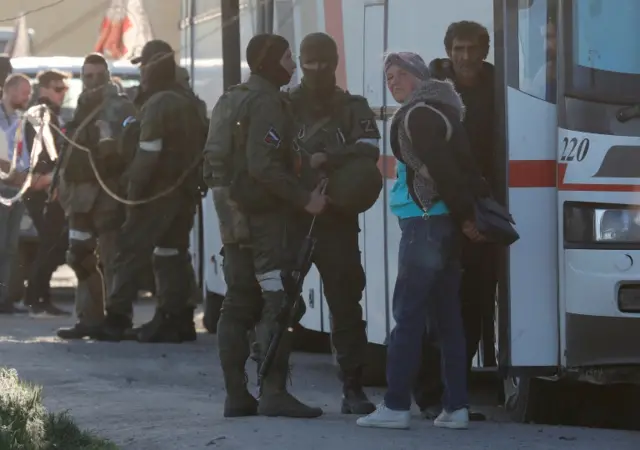 Service members of pro-Russian troops with civilians next to buses carrying people evacuated from Mariupol on 7 May 2022.