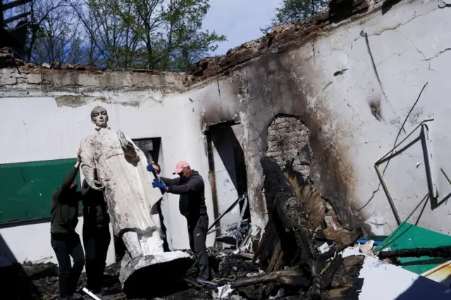 Employees remove the statue of Ukrainian philosopher Hryhoriy Skovoroda after a Russian bombing hit a local museum in the Kharkiv region