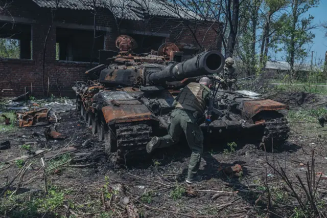 Ukrainian soldiers stand next to a destroyed Russian tank on the outskirts of Kharkiv, Ukraine