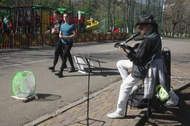 People walking in a park while a busker sings