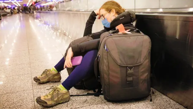 A woman with a backpack sits with her head in her hand at an airport